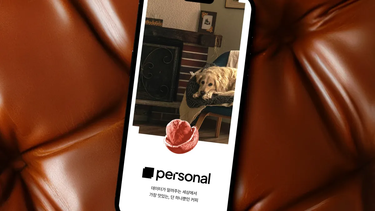 가죽 소파 위에 놓인 휴대폰에 커피 브랜드 퍼스널의 앱 화면이 보이는 사진